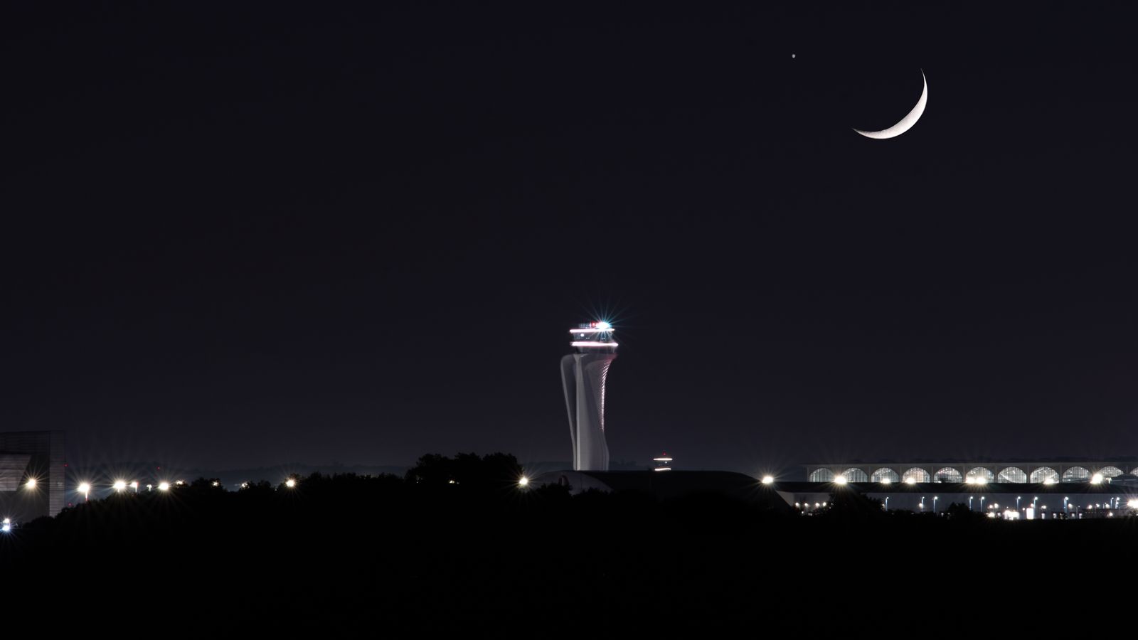 Airport control tower under a crescent moon at night